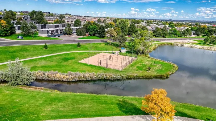Scenic aerial view of a vibrant community park with a charming pond, lush greenery, and a fenced sports court, perfect for outdoor activities and relaxation.