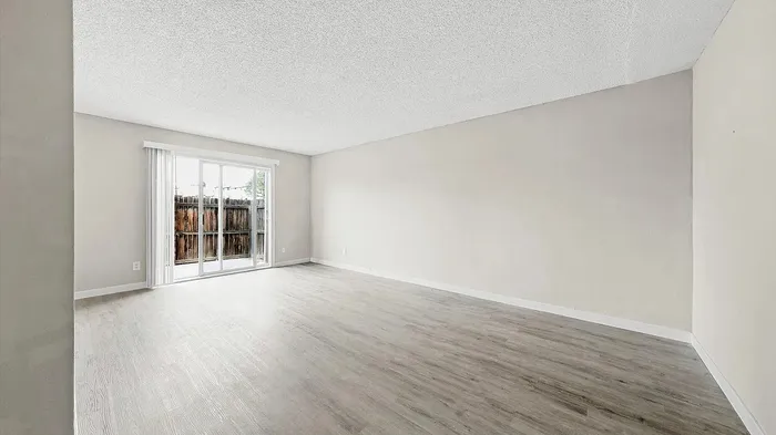 Bright, spacious living area with elegant hardwood floors and large sliding glass doors leading to a private patio.