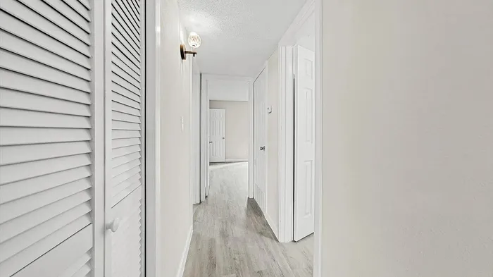 Bright and inviting hallway with modern light fixture, sleek wooden flooring, and crisp white doors, showcasing a stylish apartment interior.