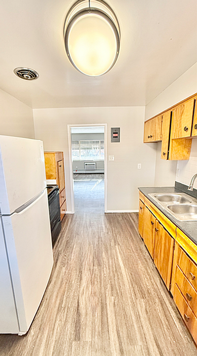 Bright and inviting kitchen with modern lighting, wooden cabinetry, and sleek countertops, leading into a sunlit living area.