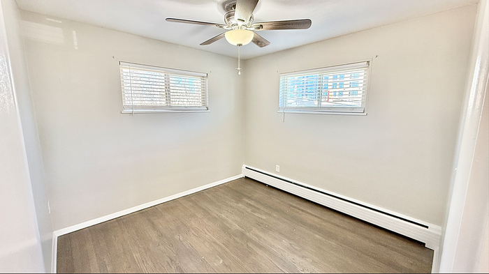 Bright and airy room with sleek hardwood floors, modern ceiling fan, and large windows offering natural light.
