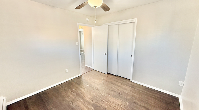 Bright and airy bedroom with sleek hardwood floors and modern ceiling fan, offering spacious closet space.