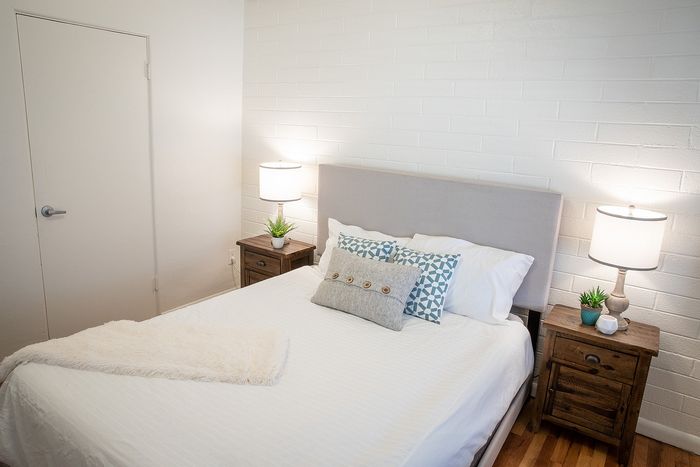 Inviting bedroom with a cozy bed, stylish pillows, and elegant wood nightstands, illuminated by soft lighting.