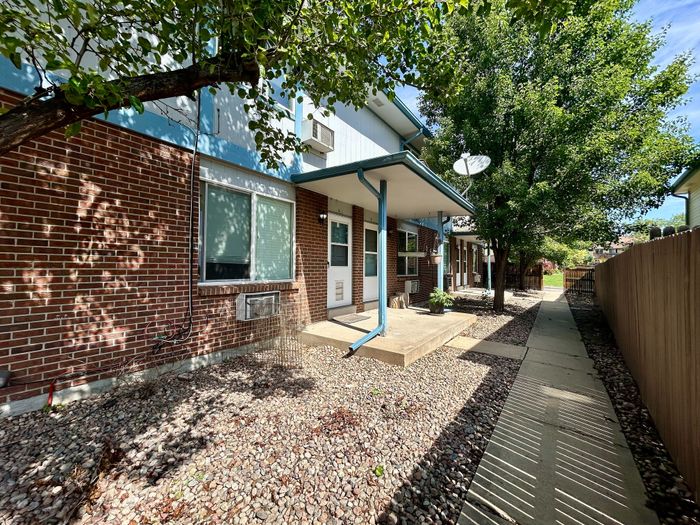 Charming brick apartment exterior with lush greenery and a cozy concrete patio.
