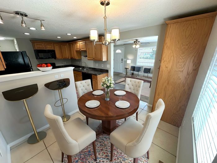 Chic dining area with round wooden table, stylish chairs, and modern kitchen overlooking living space.