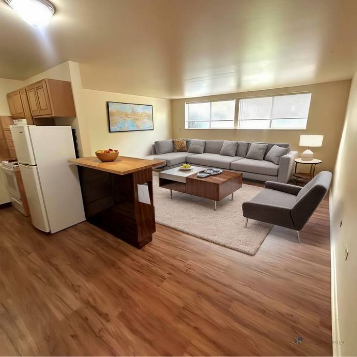 Inviting open-concept living room with stylish furniture, wooden flooring, and large windows.