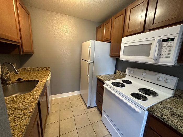 Compact kitchen with granite countertops, white appliances, and wood cabinetry.