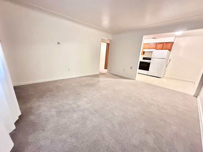 Bright and inviting living room with plush carpeting, seamlessly connecting to a cozy kitchen area.
