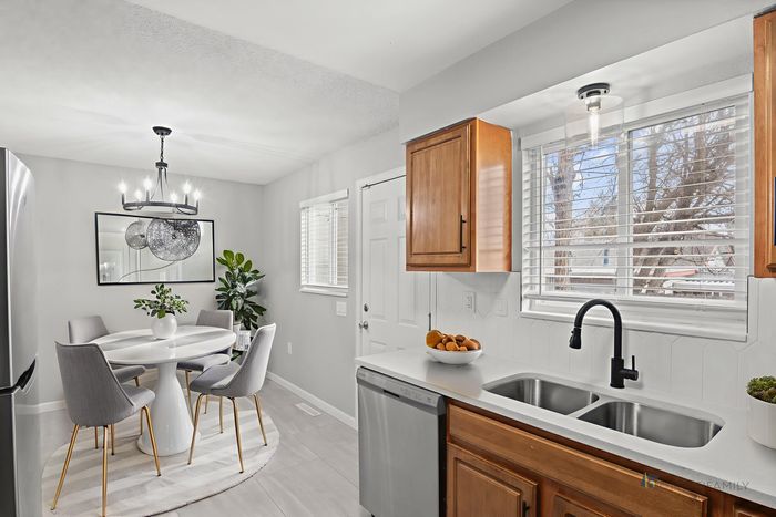 Modern dining area with round table and chic chairs, adjacent to a bright kitchen featuring wooden cabinets and a dual sink under large windows.