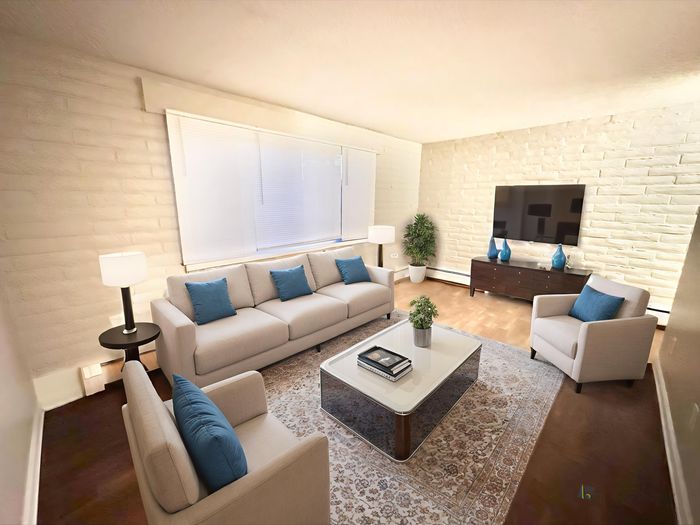 Inviting living room featuring a cozy sofa with blue accent pillows, elegant armchairs, large flat-screen TV, and ambient lighting.