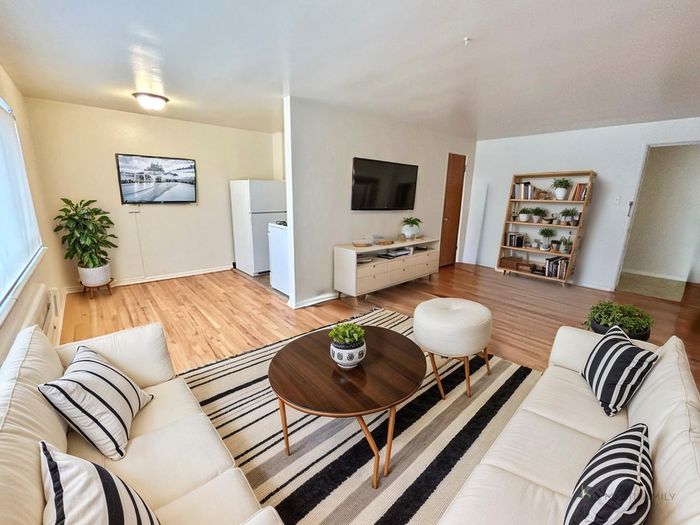 Inviting living area with stylish decor, featuring a cozy cream sofa, wooden coffee table, and decorative plants, complemented by a wall-mounted TV and bookshelf.