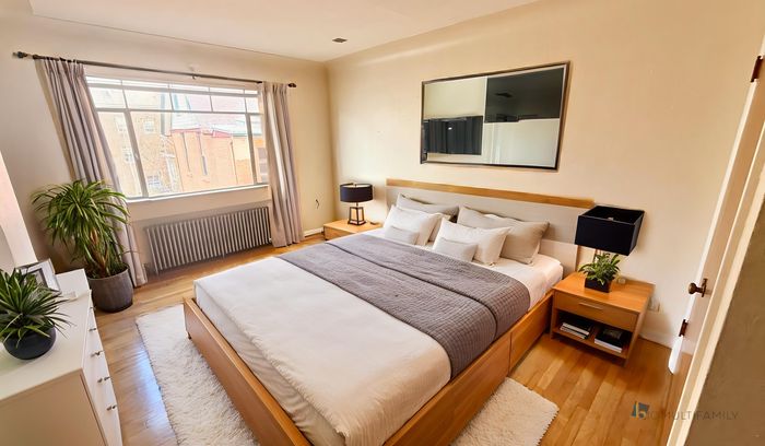 Bright and inviting bedroom with modern decor, featuring a large window, cozy bedding, and stylish wooden furniture.