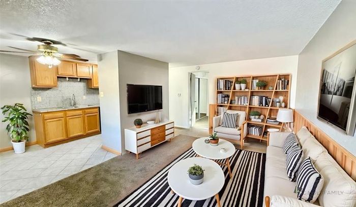 Bright and inviting living space with cozy seating, modern decor, and an adjacent kitchen featuring warm wooden cabinetry.