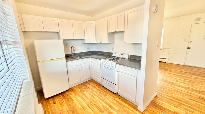 Bright, modern kitchen with sleek white cabinetry, compact appliances, and stylish hardwood flooring.