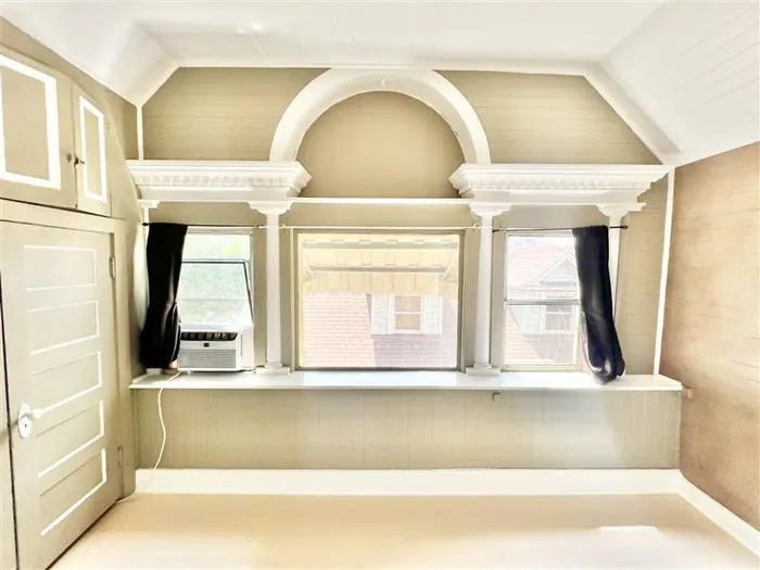 Beautiful room with classic arch details and built-in shelf space beneath a large window, offering ample natural light and charming architectural character.