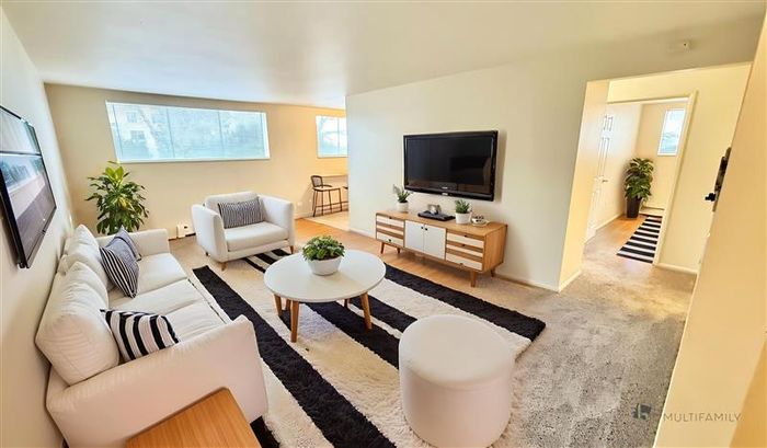 Bright and inviting living room with modern furnishings, large windows, and access to an adjoining room. Ideal for relaxation and entertainment.