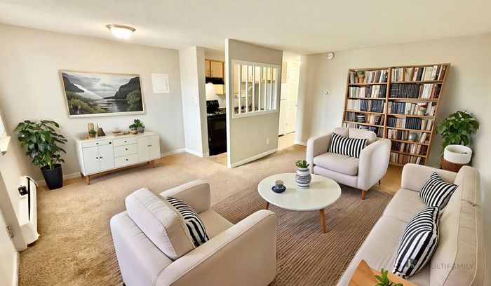 Spacious living room with modern decor, cozy seating area, and stylish bookshelf. Open access to the kitchen adds a touch of elegance.