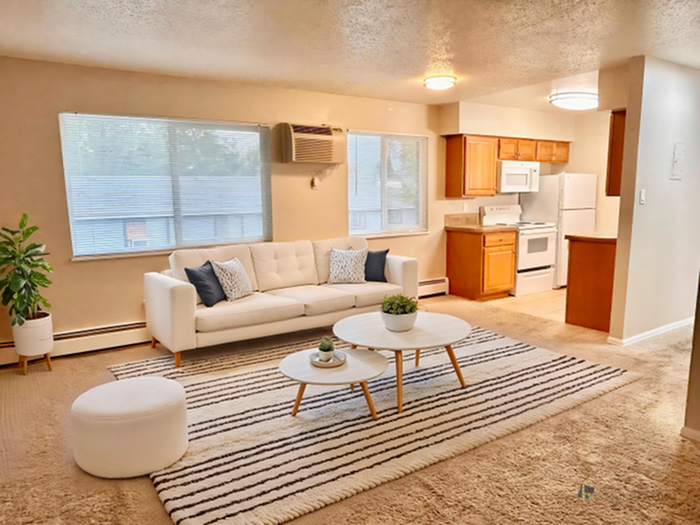 Inviting living room with stylish white sofa, cozy area rug, and modern coffee tables, adjacent to a compact kitchen with wooden cabinetry and white appliances.