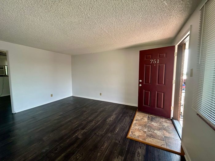 Inviting apartment interior featuring rich dark wood flooring and an elegant maroon door, perfect for a welcoming entrance.