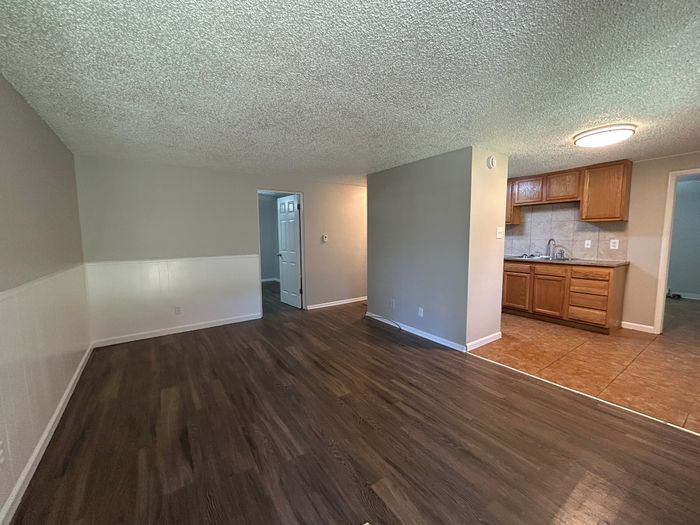 Cozy apartment interior featuring an open living area with elegant wood flooring, adjacent to a compact kitchen with warm wooden cabinetry.