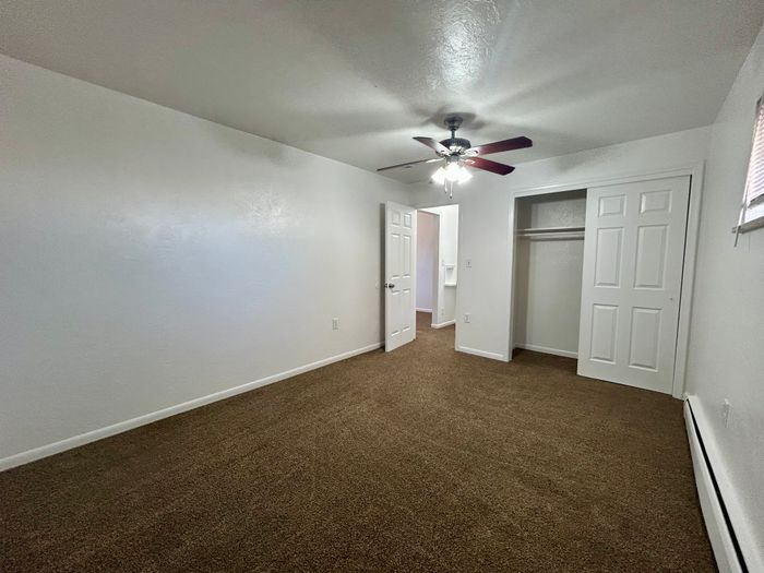 Bright and inviting bedroom with plush carpeting, ceiling fan, and ample closet space, ideal for comfort and relaxation.