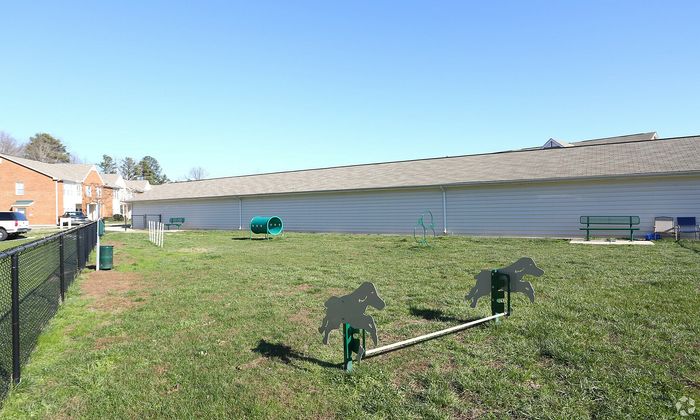 Sunny dog park with agility equipment and grassy play area beside modern townhouses.