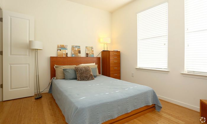 Bright bedroom with stylish wooden furniture, soft bedding, and ample natural light from two large windows.