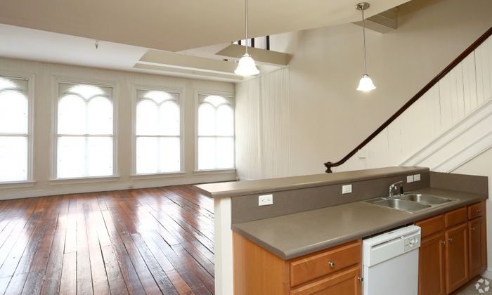 Spacious loft apartment with large arched windows and sleek kitchen counter.