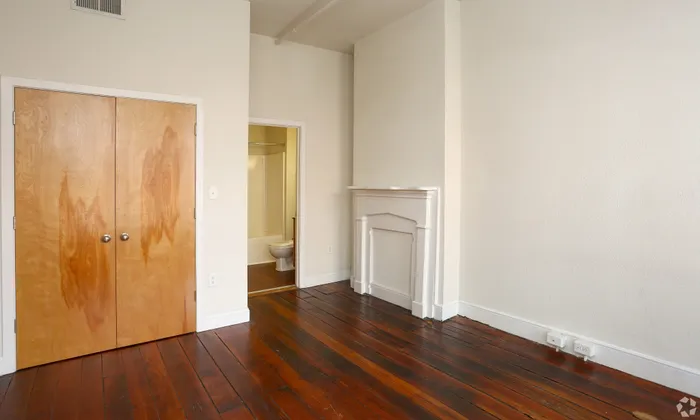 Inviting bedroom with hardwood floors, wooden closet doors, and a white fireplace mantel.