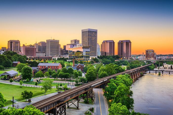 Breathtaking sunset cityscape featuring a skyline of modern buildings surrounded by lush greenery and a tranquil river.