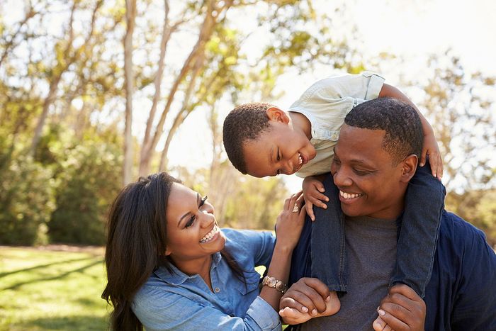 Happy family enjoying time together outdoors, with the child playfully sitting on the father's shoulders.