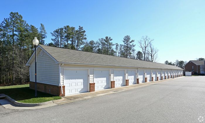 Long row of modern garage units with white doors, set against a backdrop of tall trees and clear blue sky.