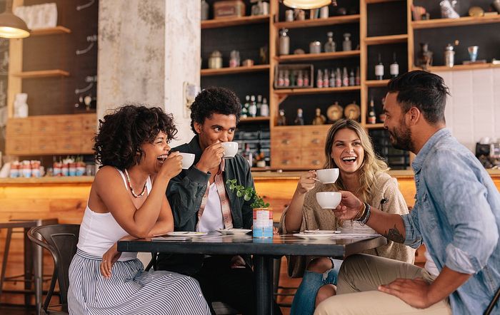 Four friends enjoying coffee together in a cozy caf&eacute; setting.