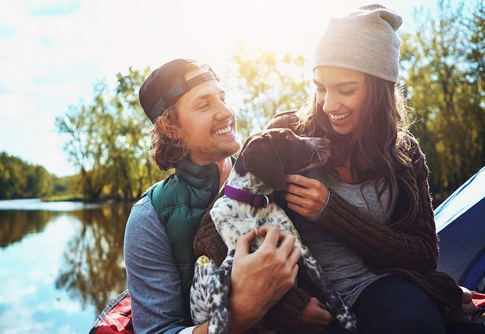 Couple enjoying a relaxed moment by the lake with their playful dog, under a sunny sky.