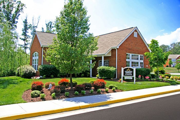Brick clubhouse surrounded by well-maintained landscaping and lush greenery on a sunny day.