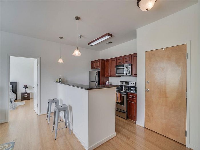 Modern apartment kitchen with sleek stainless steel appliances, bar seating, and hardwood floors.