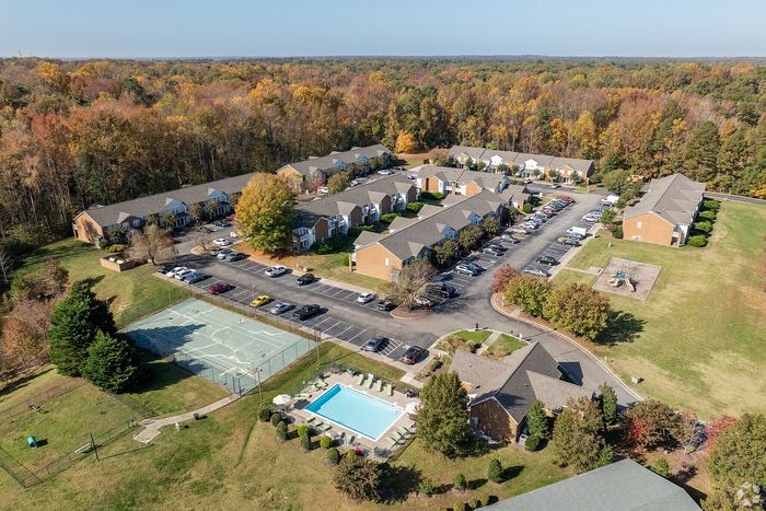 Aerial view of a residential community with well-maintained apartments, a swimming pool, tennis court, parking area, and vibrant fall foliage surrounding the area.