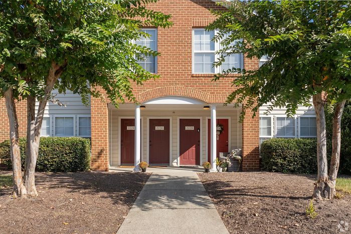 Inviting entrance of a brick townhouse with red doors and a manicured walkway.