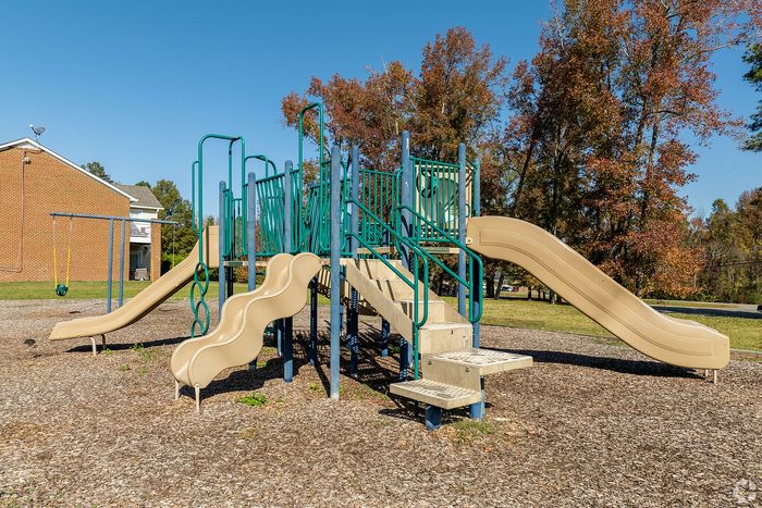 Bright and inviting playground with multiple slides and climbing structures surrounded by autumn trees.