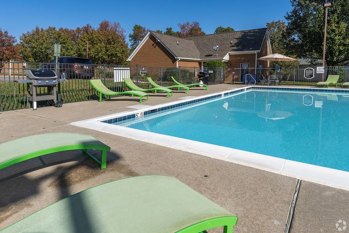 Inviting outdoor pool area with vibrant green lounge chairs and a barbecue grill, set against a backdrop of lush trees and a cozy clubhouse.
