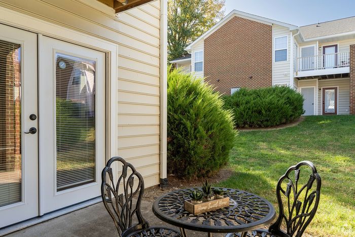 Cozy patio with decorative table set and lush greenery next to beautiful apartment exterior.
