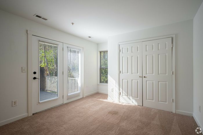 Spacious bedroom with plush carpeting, French doors leading to a balcony, and ample closet space.