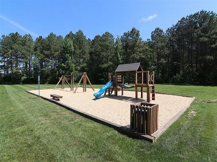 Charming outdoor playground with swings, slide, and climbing structure surrounded by lush greenery.