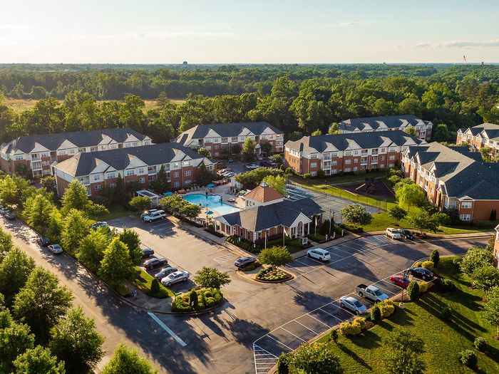 Aerial view of a picturesque apartment complex with lush greenery and a central swimming pool.