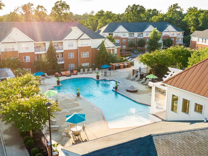 Vibrant aerial view of a sunlit pool surrounded by lush greenery and elegant apartment buildings.