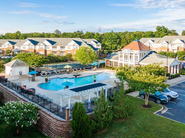 Elegant apartment complex with a large swimming pool and lush greenery, featuring modern architecture and vibrant amenities.
