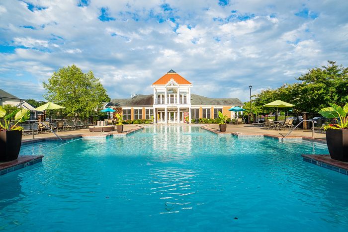 Inviting swimming pool in front of a stylish clubhouse, surrounded by lush greenery and sun loungers.