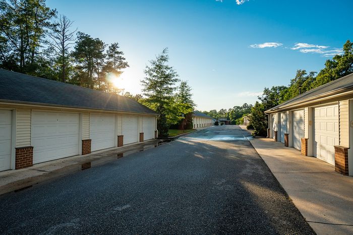 Charming row of garages with sunlit trees and clear sky, offering ample parking space.