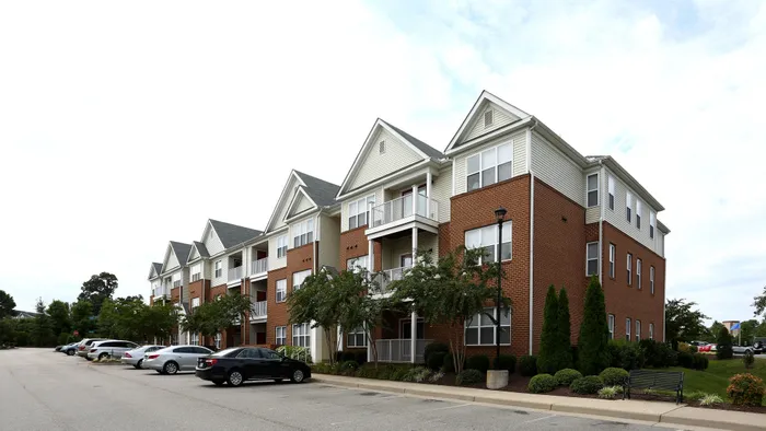 Elegant multi-story brick and siding apartment complex with balconies and lush landscaping.