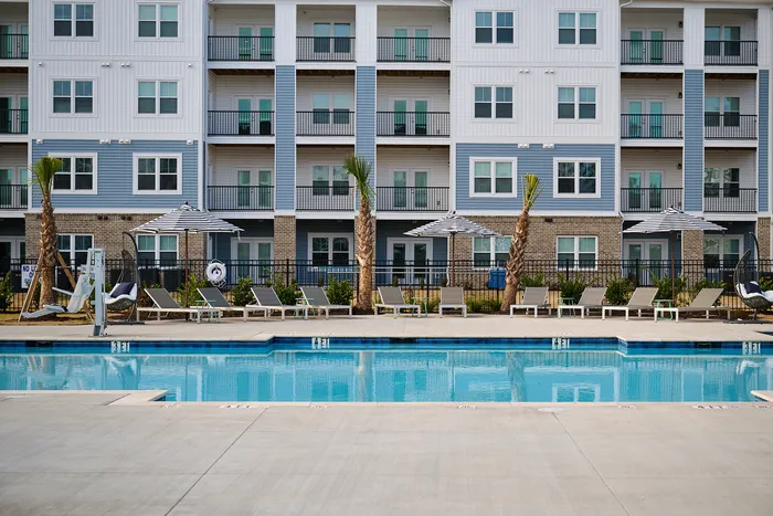 Chic apartment building facade with a pristine pool and comfortable sun loungers.